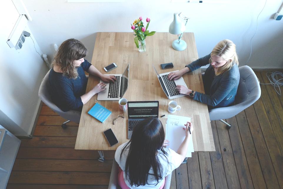 three women sitting around table using laptops